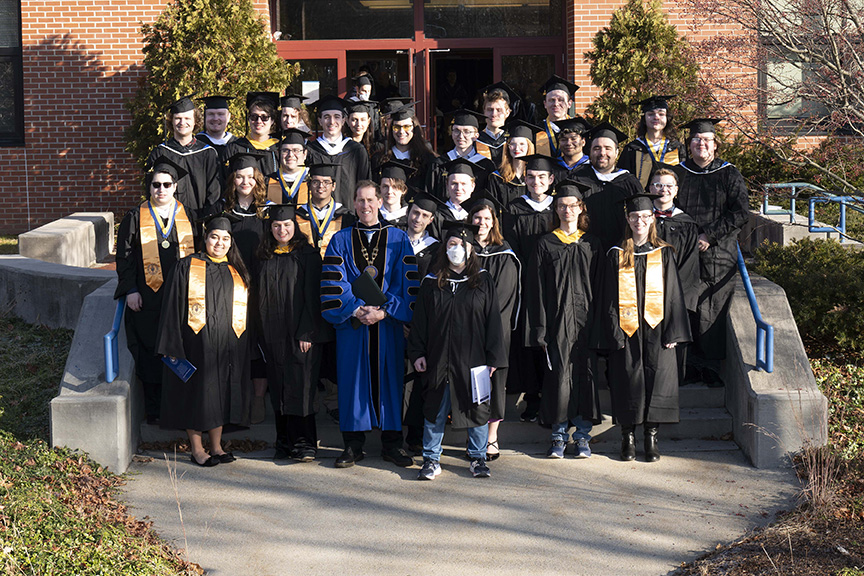 Group picture of December 2023 graduates with President Dr. Peter Eden out in front of the Click Family Sports Center 
