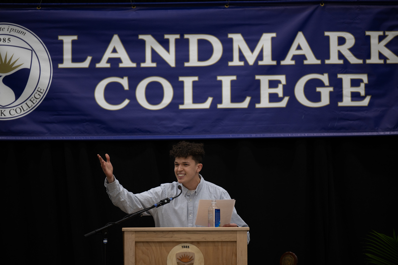 Picture of male student at podium gesturing with his right hand 