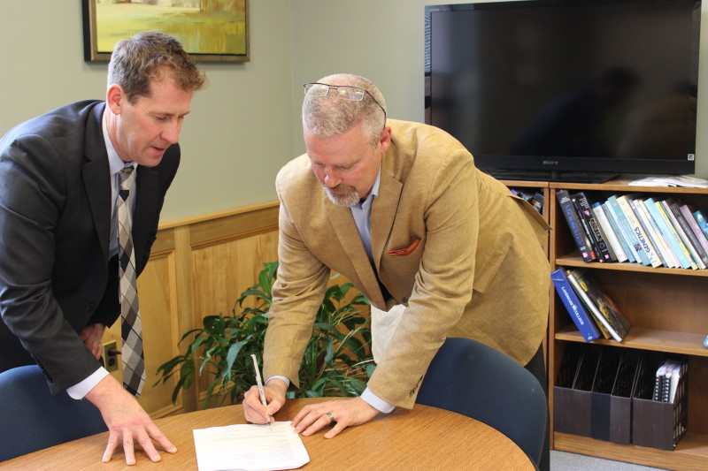 Dr. Peter Eden looks on as Bob Brown signs paper at table