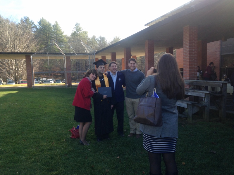 Four people, including a new graduate, pose as a woman takes their photo outside on the Landmark College quad