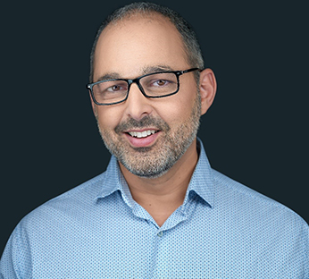 Headshot of Dr. Cyrus Shaoul. He has thin grey hair and beard and is wearing glasses and a blue shirt